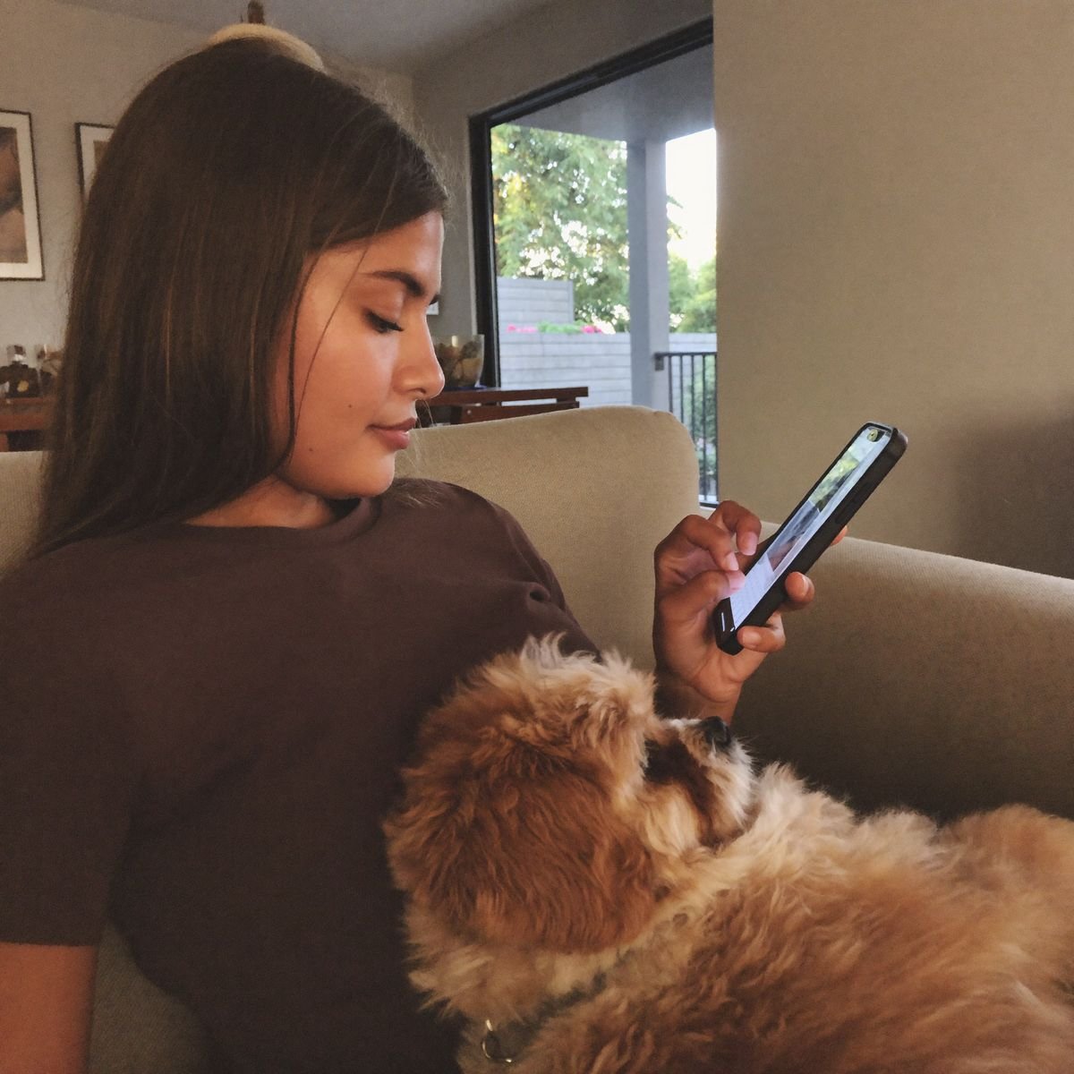 Tutora mandando mensagem pelo celular com o cachorro no colo