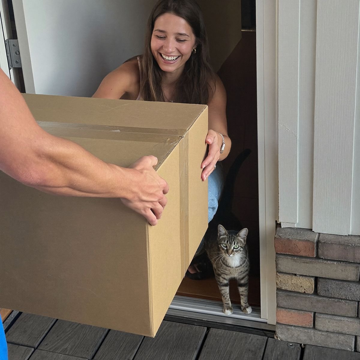 Cliente recebendo a entrega na porta de casa com o gato espiando